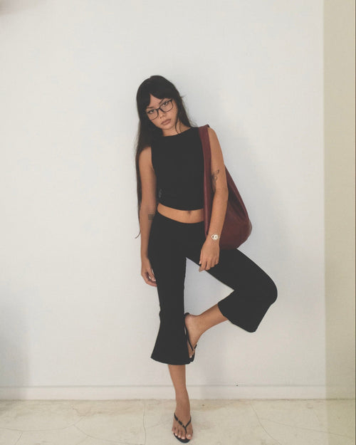 Woman in black outfit with a red bag against a white wall