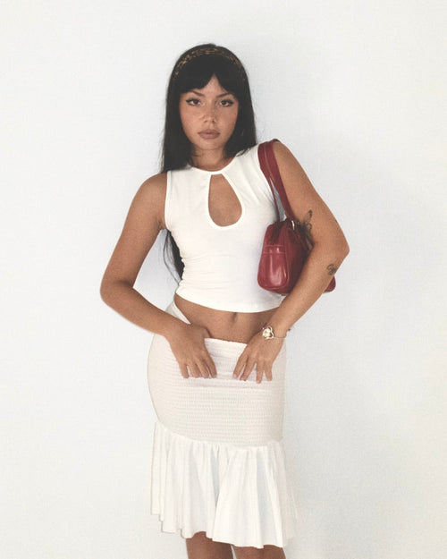 Woman wearing a white sleeveless top and skirt with a red handbag on a plain background